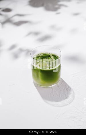 Erfrischende Eismatcha Latte sitzt auf einem weißen Tisch mit Schatten von Blättern im Hintergrund Stockfoto