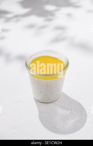 Glas mit gesundem Tapiokapudding Dessert mit Mangopüree auf weißem Tisch mit Schatten Stockfoto
