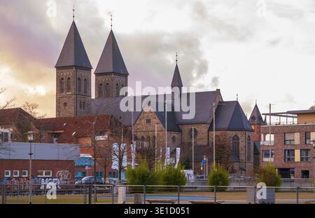 Eine majestätische romanische Kirche mit zwei Steintürmen und konischen Dächern dominiert die Skyline einer europäischen Stadt. Die historische Architektur steht im Kontrast zu wi Stockfoto