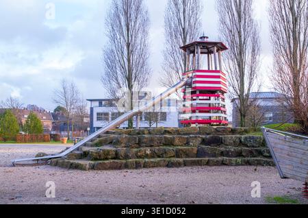 Kreative Spielplatzstruktur mit markantem rot-weiß gestreiften Turm mit Rutsche, auf Steinfundament in urbanem Park mit Tre gebaut Stockfoto