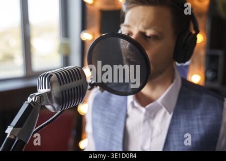 Ein junger gutaussehender bärtiger Mann singt in ein Mikrofon in einem Musikstudio Stockfoto