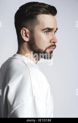Hübscher bärtiger Mann mit weißem Sweatshirt auf grauem Hintergrund Stockfoto