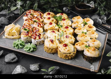 Wunderschön angeordnete Platte mit verschiedenen Sushi-Brötchen, garniert mit Gemüse, serviert auf einem dunklen Steintisch Stockfoto