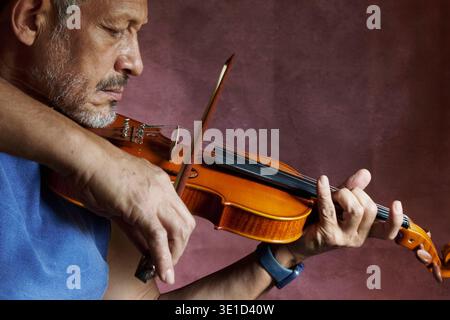 Reifer erwachsener Mann, der Violine spielt und sich auf die Musik und sein Instrument konzentriert Stockfoto