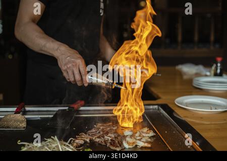 Hände des Küchenchefs mit Spachtel über Teppanyaki. Kochen von Gemüse, Fleisch und Meeresfrüchten auf heißem Hibachi-Grilltisch. Traditionelle Japanische Küche. Teppan Show Stockfoto