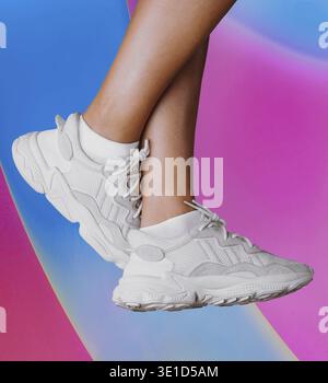Frau mit trendigen weißen Sneakers, die sich über einem leuchtenden mehrfarbigen Hintergrund posiert Stockfoto