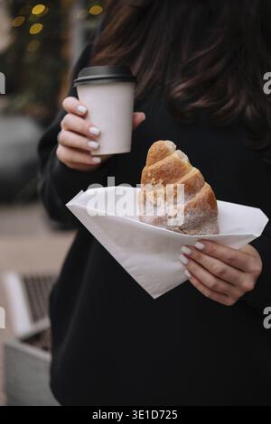 Nahaufnahme einer Frau, die ein köstliches Gebäck und warmen Kaffee in einer gemütlichen Umgebung im Freien genießt Stockfoto