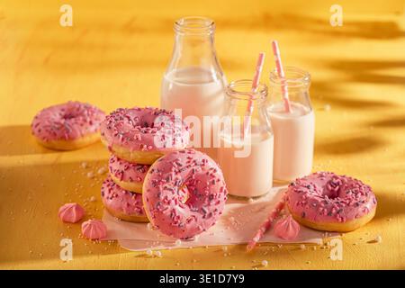Frische und leckere rosa Donuts serviert mit Milch in der Flasche. Serviert mit Milch auf gelbem Tisch. Beliebtestes Dessert. Stockfoto
