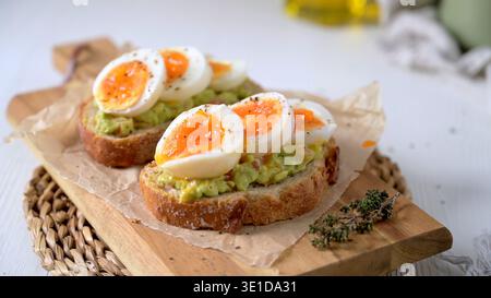 Zwei Scheiben knuspriges Sauerteigbrot, garniert mit cremiger Guacamole und weichen, gekochten Eierhälften. Warmes natürliches Licht unterstreicht den lebendigen Orang Stockfoto