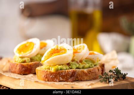 Zwei Scheiben knuspriges Sauerteigbrot mit cremigem Avocadopüree und perfekt weich gekochten Eiern. Warmes natürliches Licht hebt das Marmeladyolk hervor Stockfoto
