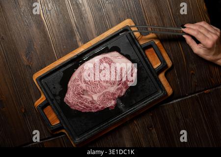 Marmoriertes Wagyu Ribeye Steak auf einer rechteckigen gusseisernen Platte mit Holzsockel. Das Fleisch weist eine komplizierte Marmorierung auf, was für seine erstklassige Qualität spricht Stockfoto