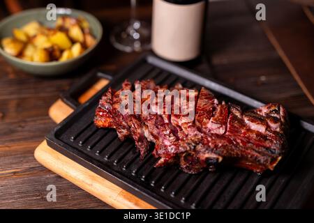 In einer gusseisernen Pfanne auf einem Holztisch befindet sich ein mittelseltenes Rindersteak, das in rötlich-rosa Tönen gekocht wird. In der Nähe gibt es eine Schüssel mit gegrilltem Stockfoto