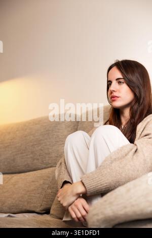Junge Frau, die zu Hause im gemütlichen Wohnzimmer nachdenkt Stockfoto