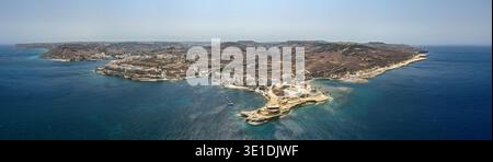 Panoramablick auf die Bucht von Xwejni mit felsiger Landzunge, türkisfarbenem Untiefen, Apartments an der Küste, terrassiertem Ackerland und verankerten Booten auf Gozo, Malta. Stockfoto