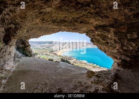 Blick von der Mixta Cave in Nadur, Gozo, mit Blick durch die Felsöffnung in Richtung Ramla Buys türkisfarbenes Wasser und Sandstrand. Stockfoto