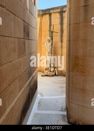 Steinstatue mit einem Kreuz in einer schmalen Kalksteinpassage in der Rotunde der St. Johannes-Täufer-Kirche, Xewkija, Gozo, Malta. Stockfoto