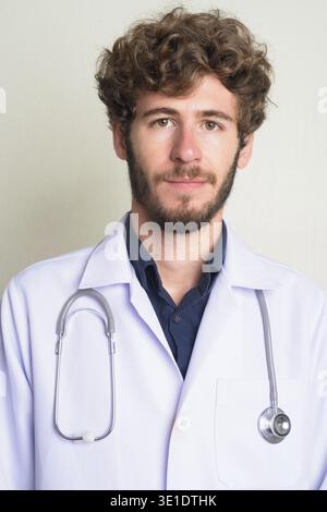 Studio-Aufnahme eines jungen gutaussehenden bärtigen Mannes Doktor mit lockigen Haaren vor weißem Hintergrund Stockfoto