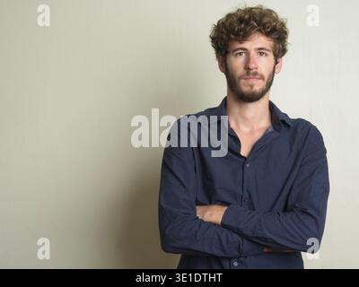 Studio-Aufnahme eines jungen gutaussehenden bärtigen Geschäftsmannes mit lockigen Haaren vor weißem Hintergrund Stockfoto