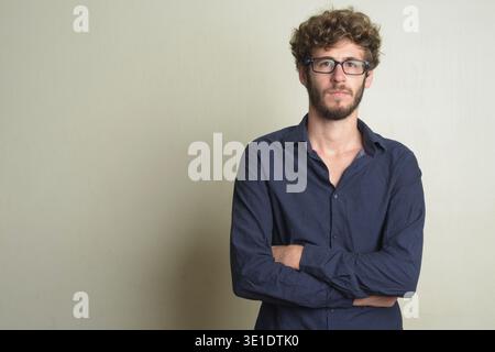 Studio-Aufnahme eines jungen gutaussehenden bärtigen Geschäftsmannes mit lockigem Haar, der eine Brille vor weißem Hintergrund trägt Stockfoto