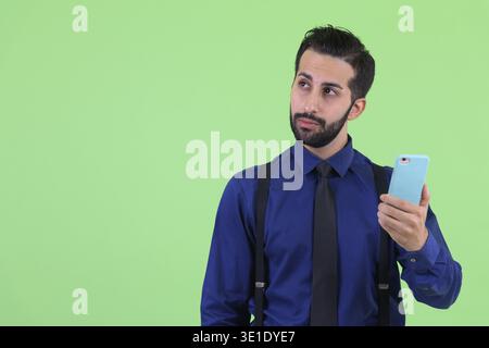 Studio-Aufnahme eines jungen gutaussehenden, bärtigen persischen Geschäftsmannes vor grünem Hintergrund Stockfoto