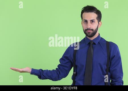 Studio-Aufnahme eines jungen gutaussehenden, bärtigen persischen Geschäftsmannes vor grünem Hintergrund Stockfoto