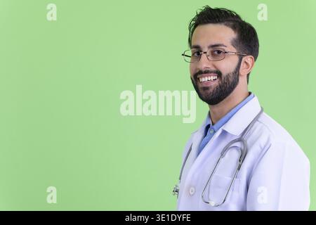 Studio-Aufnahme eines jungen gutaussehenden, bärtigen persischen Mannes Doktor vor grünem Hintergrund Stockfoto