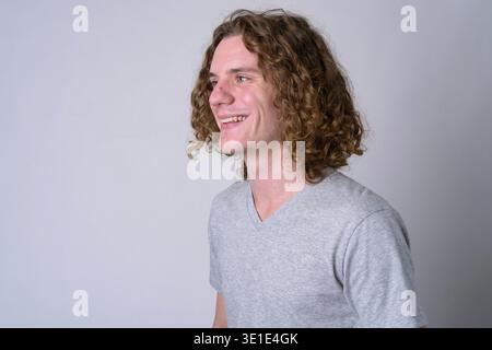 Studio-Aufnahme eines jungen, gutaussehenden Mannes mit langen lockigen Haaren vor weißem Hintergrund Stockfoto