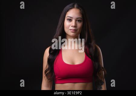 Studio-Aufnahme einer jungen, schönen Multi-Ethno-Frau, die für das Fitnessstudio bereit ist, vor schwarzem Hintergrund Stockfoto