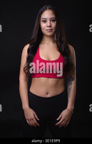 Studio-Aufnahme einer jungen, schönen Multi-Ethno-Frau, die für das Fitnessstudio bereit ist, vor schwarzem Hintergrund Stockfoto
