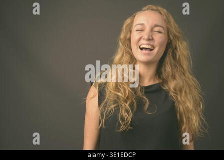 Studio-Aufnahme von jungen schönen Geschäftsfrau mit langen welligen Blondine Haare vor grauem Hintergrund Stockfoto