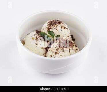 Drei Messlöffel Vanilleeis mit Schokoladenspänen und einem Minzzweig in einer weißen Schüssel serviert Stockfoto