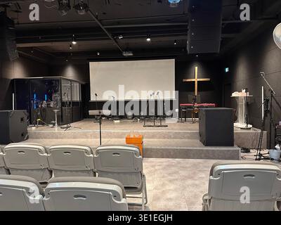 Moderne Kircheneinrichtung mit leerer Bühne für Gottesdienste, mit Musikinstrumenten, Mikrofonen, Projektorleinwand und Holzkreuz Stockfoto