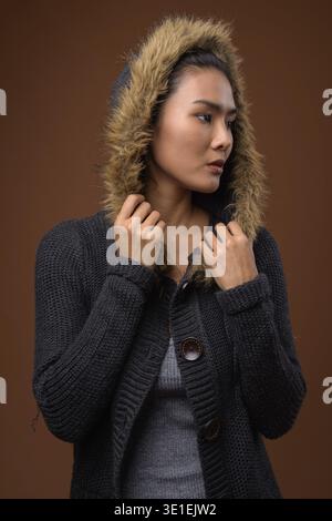 Studio geschossen von schöne asiatische Frau Wintermantel gegen braunen Hintergrund Stockfoto