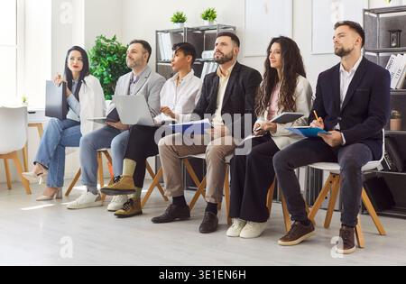 Junge Geschäftsleute, die beim Treffen im Büro hintereinander sitzen und ihren Kollegen zuhören Stockfoto