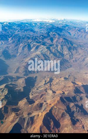 Ein Blick aus der Vogelperspektive fängt das weite, zerklüftete Gelände einer Bergkette ein und zeigt seine vielfältigen Texturen und Farben unter einem klaren blauen Himmel. Stockfoto