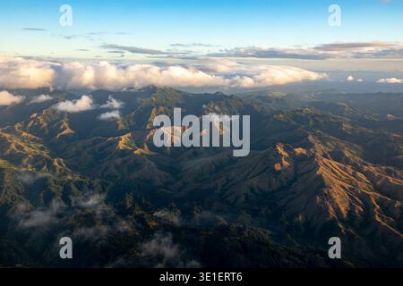 Ein Blick aus der Vogelperspektive auf zerklüftete, sonnenverwöhnte Berge unter einem hellblauen Himmel mit verstreuten Wolken. Stockfoto