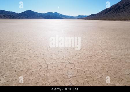 Ein riesiger, zerrissener Schlammboden erstreckt sich zu weit entfernten Bergen unter einem klaren blauen Himmel. Die trockene, vertrocknete Erde ist ein Mosaik aus polygonalen Formen, Indicatin Stockfoto