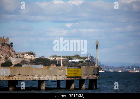 In der Nähe von Alcatraz Island, San Francisco, Kalifornien, fliegt ein Vintage-Jet-Kampfflugzeug über dem Wasser. Das Flugzeug ist silber mit gelben und roten Akzenten und Stockfoto
