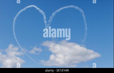 Ein Flugzeug zeichnet eine Herzform am Himmel mit einer Rauchspur und hinterlässt ein Symbol der Liebe auf der blauen Weite. Stockfoto