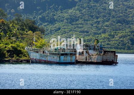 Die Schiffe „HARI“ und „KIDRON-II HONIARA“ liegen in einer Bucht mit einem üppig grünen, bewaldeten Hügel im Hintergrund. Die Schiffe scheinen verlassen zu sein und A Stockfoto