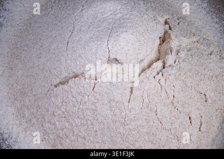 Zerbrochenes Mehl in Holzschale. Handwerklicher Arbeitsbereich mit weichen Schatteneffekten. Detaillierte Ansicht des Mehls, das während der Teigherstellung in einer Holzschale gerissen wurde Stockfoto