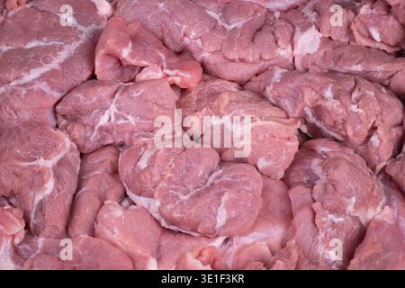 Übereinander gestapelte Schweinefleisch-Schnitte, ordentlich auf der Verkaufsfläche angeordnet. Frisch geschnittene Schweinestücke in hellen Regalen mit einheitlichen Portionen Stockfoto