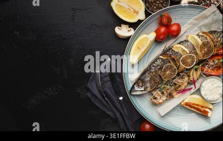 Gebratener Fisch mit Gemüse, serviert im Restaurant auf schwarzem Tisch Stockfoto