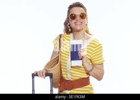 Eine fröhliche Frau in einem gelb gestreiften Kleid, bereit für einen Sommerurlaub, mit Reisedokumenten und neben ihrem Rollkoffer. Stockfoto