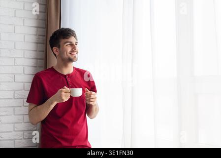 Glücklicher Mann, der eine Tasse Kaffee am Fenster hält Stockfoto