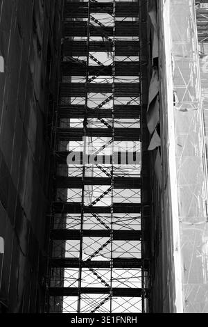 Nahaufnahme von komplexen Gerüsten und Treppenbrücken zwischen hohen Gebäuden, die industrielle Geometrie und vertikale Linien hervorheben. Stockfoto