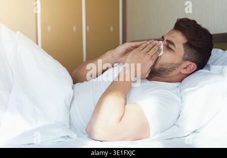 Junger Mann niest und bedeckt die Nase mit auf dem Bett liegendem Gewebe Stockfoto