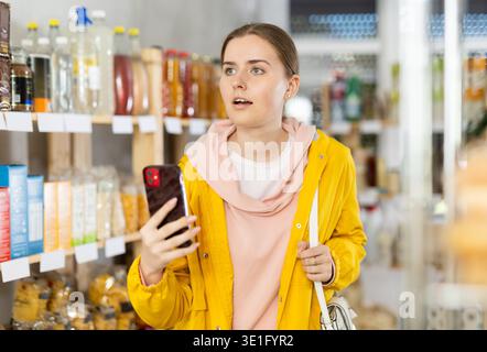Mädchen scannt QR-Code auf Produkten in Supermarktregalen, um das Ablaufdatum zu überprüfen Stockfoto