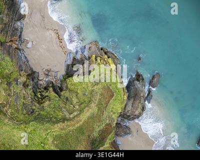 Blick aus der Vogelperspektive auf zerklüftete, grüne Klippen, die auf das türkisfarbene Meer treffen, Wellen, die sanft die Sandküste küssen, Fowey, Cornwall, Großbritannien. Stockfoto