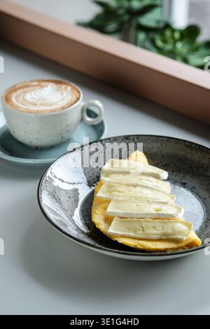 Gemütlicher Morgen Mit Dampfendem Latte Und Käse. Helle Fensterszene Mit Cremigem Kaffee Und Handwerklichem Brot Stockfoto